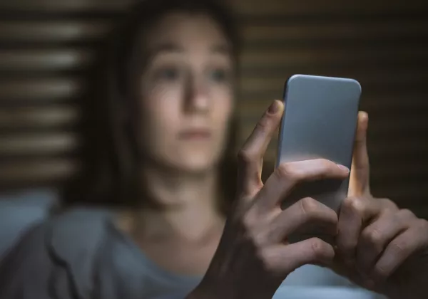Opferschutzportal Eine Frau sitzt im Dunkeln und schaut auf ihr erleuchtetes Handy-Display.